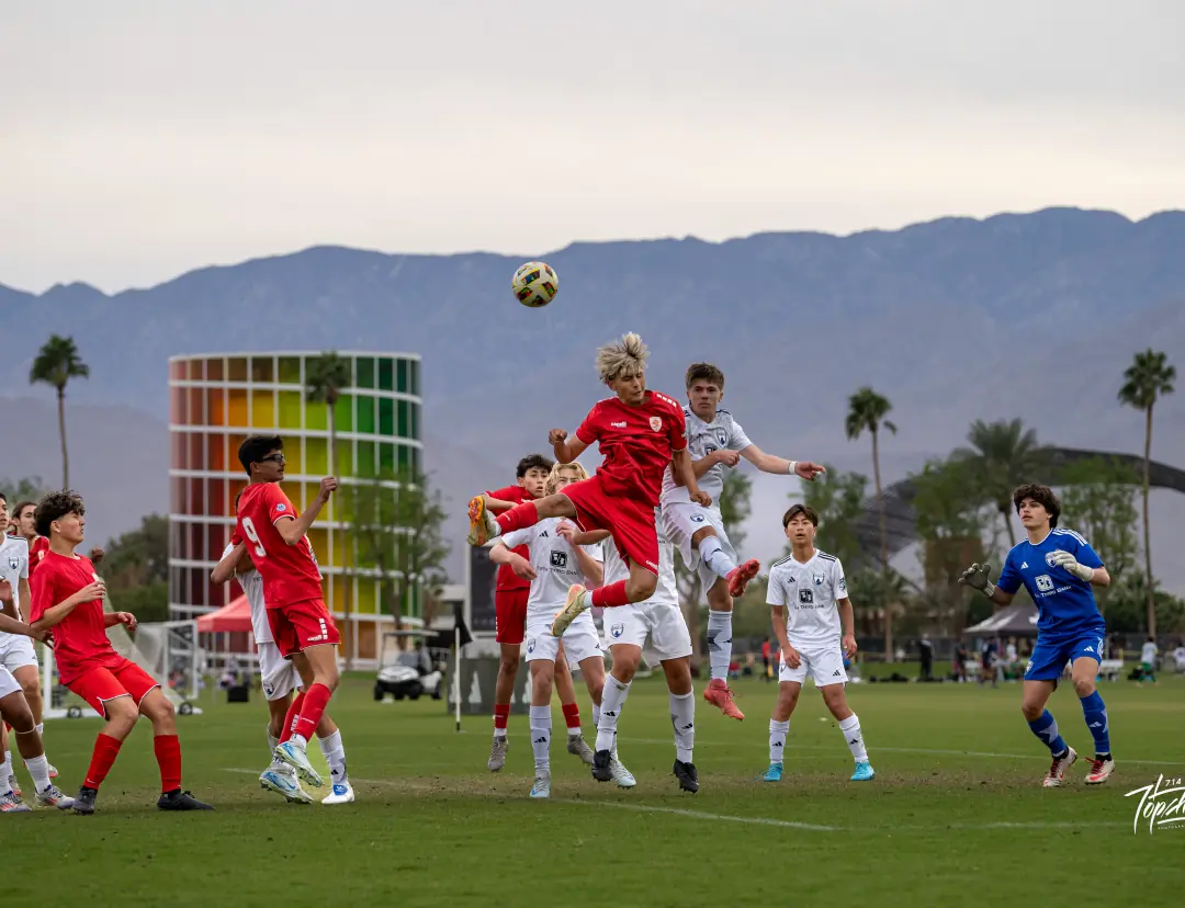 Soccer players rising for a header in front of the mountains