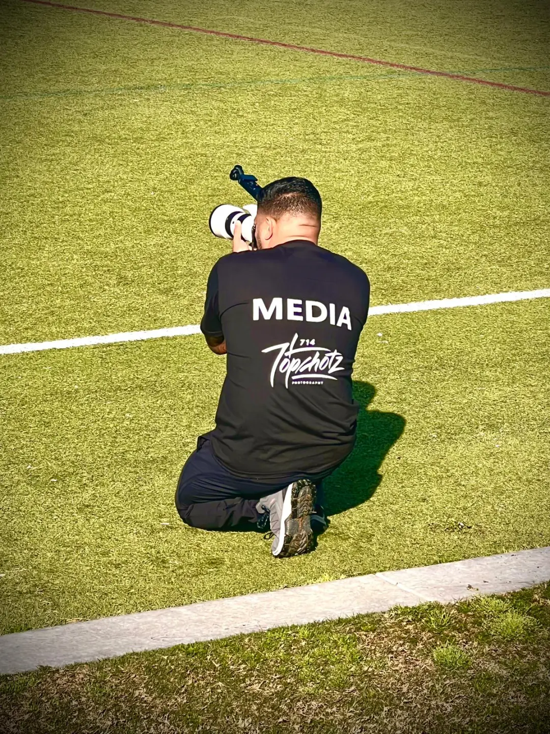 Sports photographer kneeling on the field with camera raised