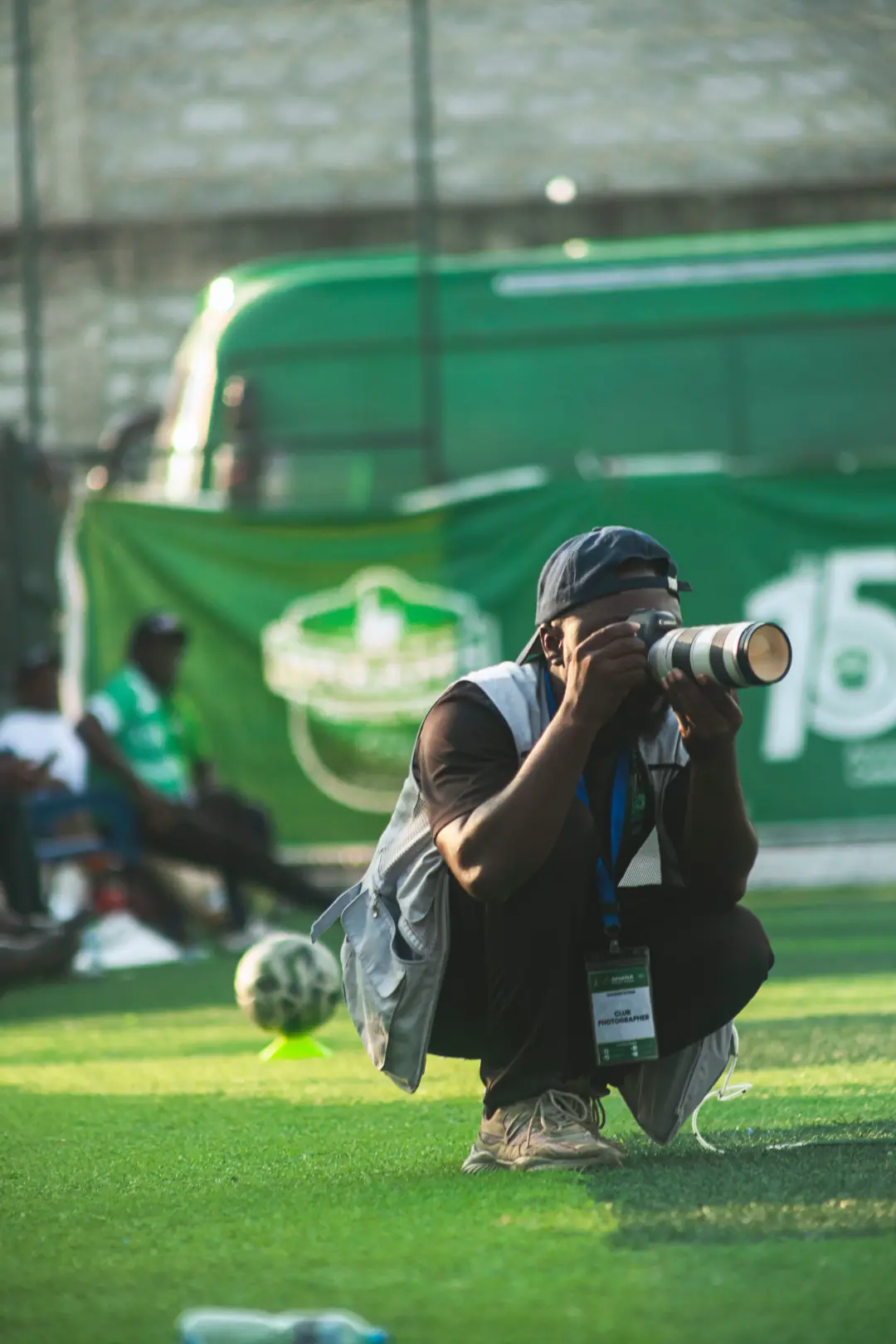Club photographer crouched on the pitch, shooting with a telephoto lens