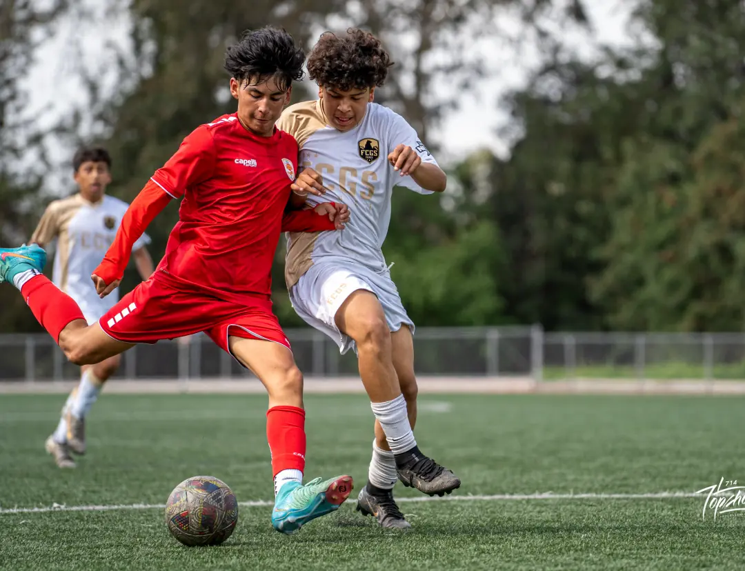 Soccer player in red striking the ball past a defender